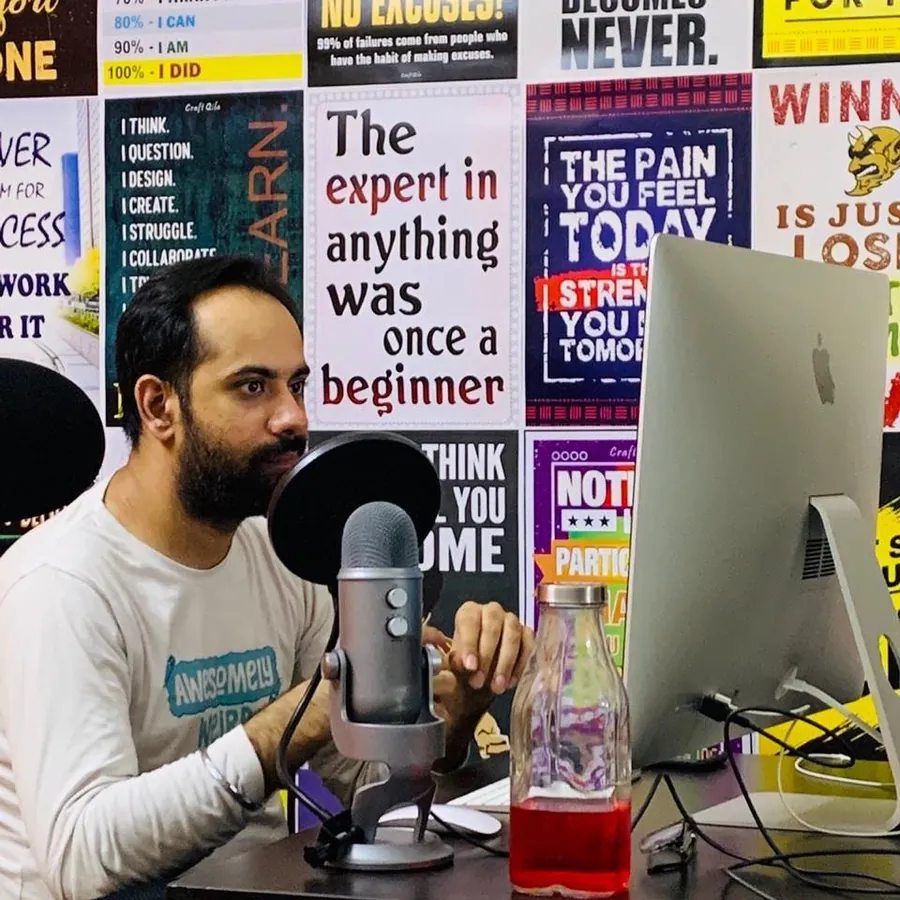 Photo: Gaurav at an iMac with a podcast microphone, a wall of motivational posters behind him